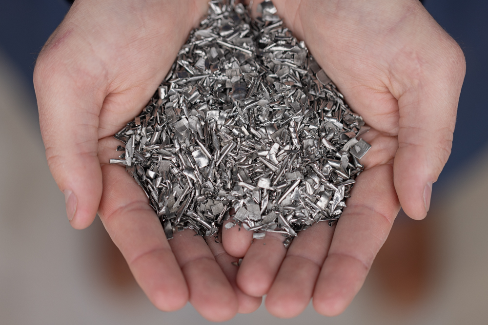 Hands cupping a pile of titanium metal scrap. IperionX's HAMR Process can take almost any form of titanium or scrap titanium alloy feedstock and produce titanium powders at very low energy intensity.
