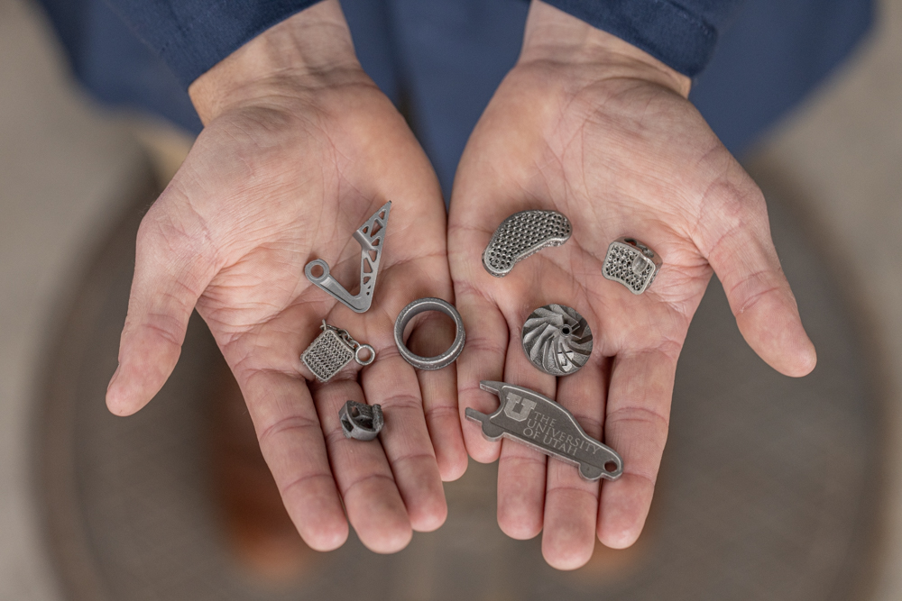 Hands holding variety of 3D printed titanium parts.