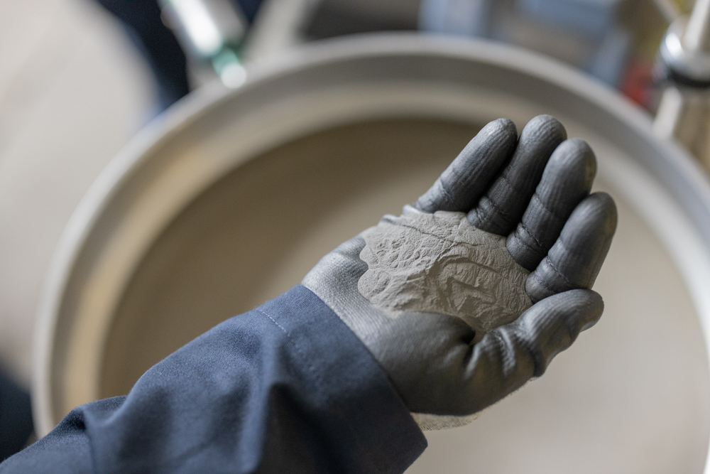 A gloved hand holds a handful of IperionX's 100% recycled titanium metal powder.