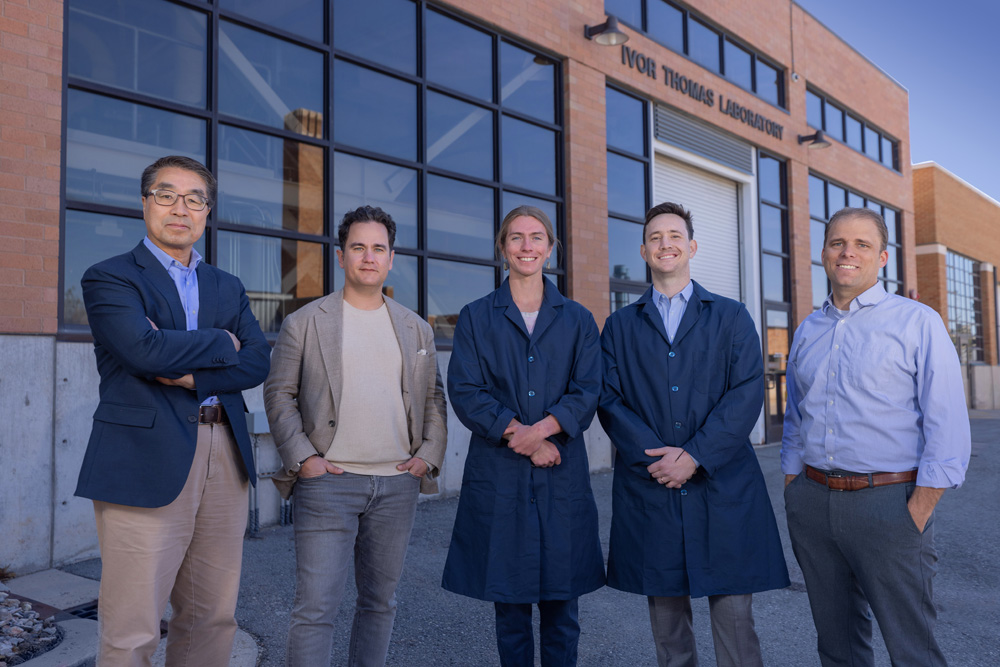 IperionX CEO, Taso Arima posting with IperionX VP of Research and Development, Hyrum Lefler, Dr. Zak Fang, and two graduate students in blue lab coats.